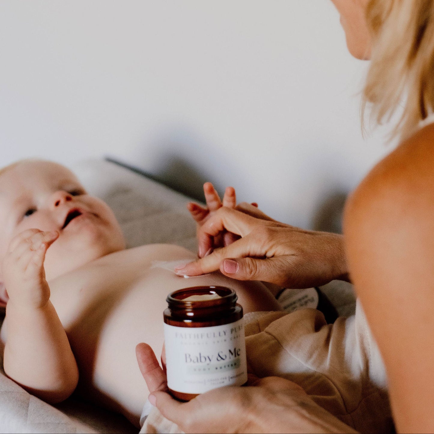 Woman holding a baby and a jar of baby lotion on a white surface