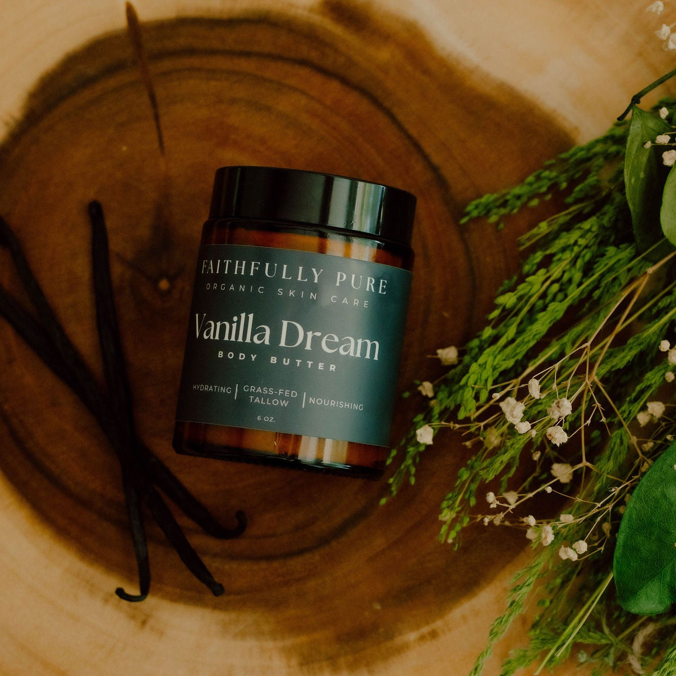 Jar of 'Vanilla Dream' body butter on a wooden surface with vanilla beans and greenery.