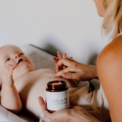 Woman holding a baby and a jar of baby lotion on a white surface