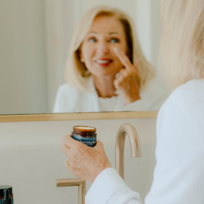 Woman applying cream to her face in front of a mirror