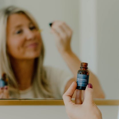 Person holding a small bottle of vtamin c serum in front of a mirror