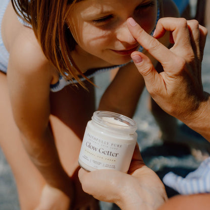 Child looking at a jar of 'Glow Getter' cream held by an adult outdoors.